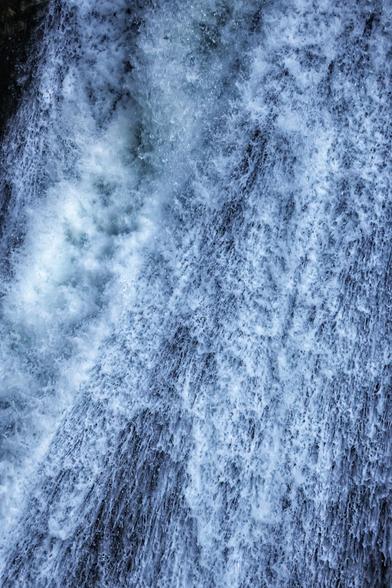 A close-up photograph of a powerful, cascading waterfall. The water appears frothy and turbulent, with intricate patterns formed by the rapid flow. The image captures the dynamic movement and texture of the water, showcasing the natural beauty and raw energy of the waterfall in vivid detail.