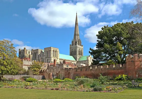 The image shows a scenic view of an old cathedral with a tall spire, set against a blue sky with some clouds. In the foreground, there is a garden with lush greenery and flowers, while the background features a historic brick wall. The architecture of the cathedral suggests it has significant historical importance.

Image Credits: Wikimedia / Evgeniy Podkopaev / CC BY-SA 3.0