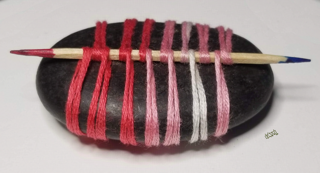Photo of a black oval stone wrapped in variegated pink embroidery thread using a paracord wrap style involving a toothpick that is pink on one end and blue on the other.