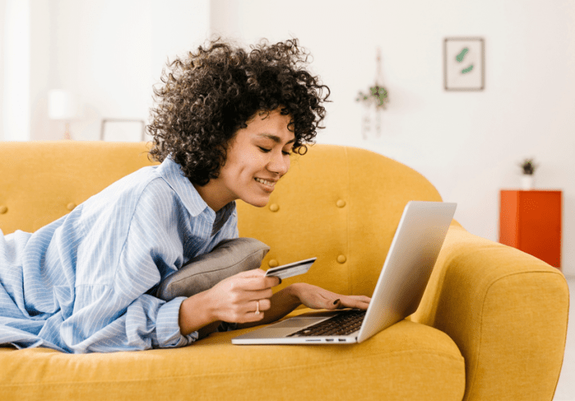 Mujer con tarjeta bancaria y computadora en sillon