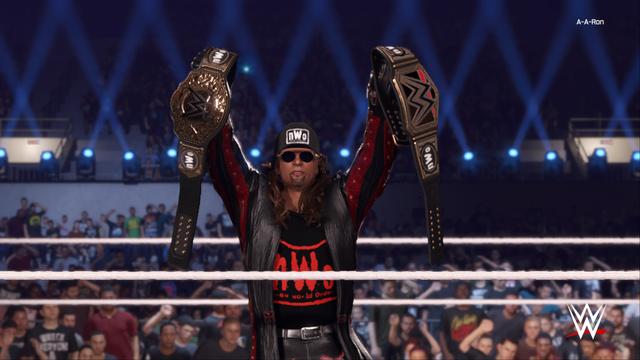 WWE wrestler in red and black ring gear holding two title belts above his head while standing inside a wrestling ring. The crowd is visible in the background, suggesting the scene takes place at an event with spectators.