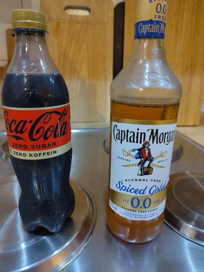 Eine Flasche Cola  ohne Koffein steht neben einer alkoholfreien Rumflasche.