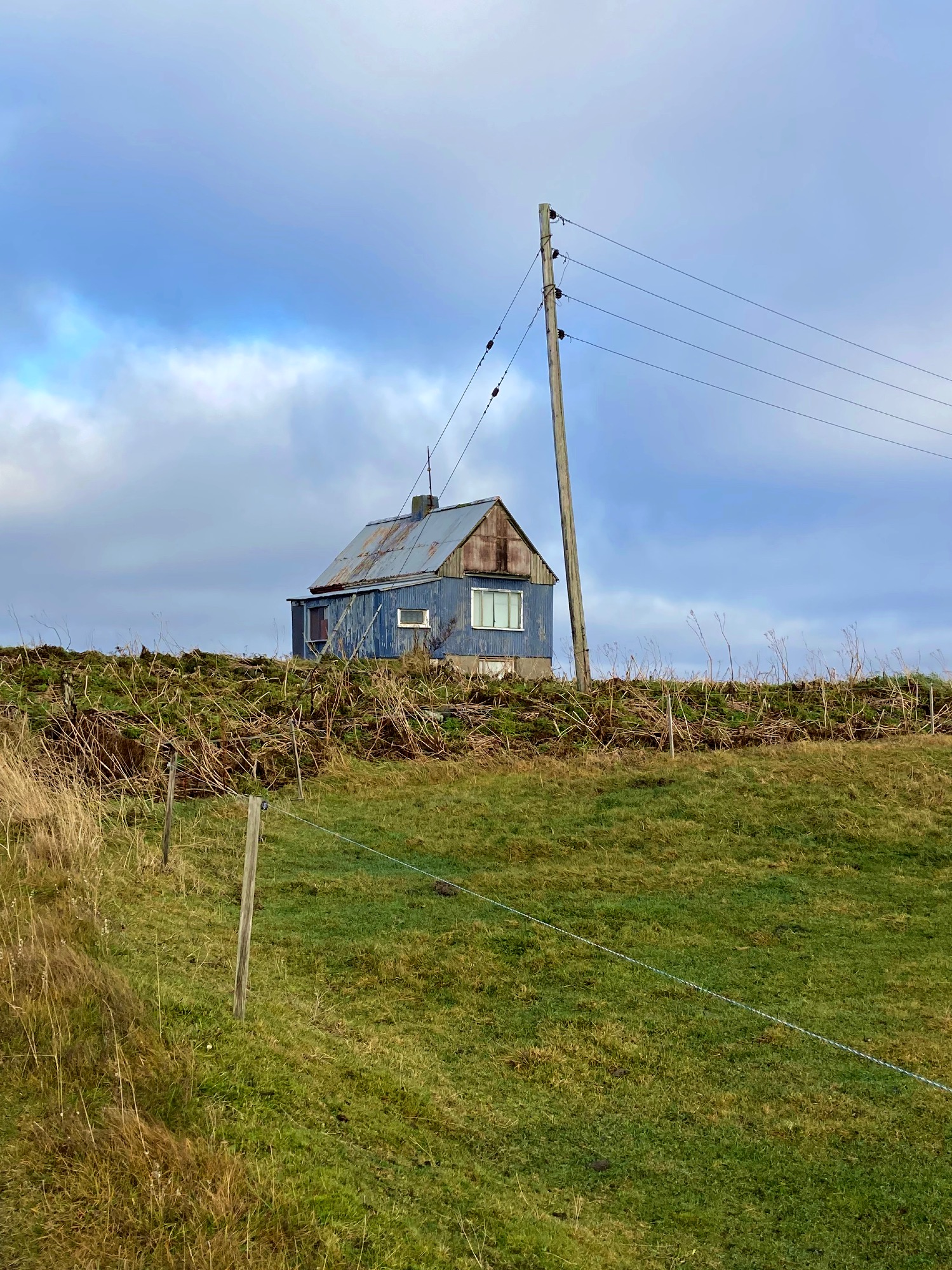 An abandoned blue house in a dilapidated condition and a tilted utility pole.