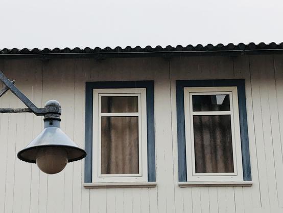 Zwei Fenster nah nebeneinander mit blauer Umrandung. Davor eine Laterne im gleichen blau.