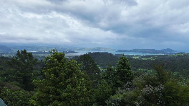 Looking down over lush temperate rainforest to a bay with islands guarding it. Threatening overcast roils above.