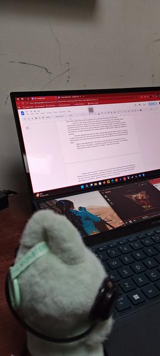 A Labubu looks over a laptop, open to a page in a book being written.