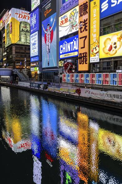 Buildings covered in bright and colourful neon commercials and reflected in the Dotonbori River in Osaka, in Japan at night.