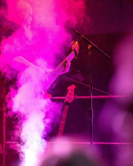 Das Bild zeigt einen Bassisten während eines Live-Auftritts, eingehüllt in hellen, magenta-farbenen Bühnennebel.
