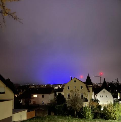 Nachtaufnahme einer blauen Lichtkuppel über der Stadt. Im Vordergrund eine Reihe Häuser.