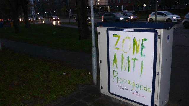 straatkastje by night met reclame bord aangepast in witte poster met verschillende kleuren groene letters, zie caption
auto rijdend op achtergrond