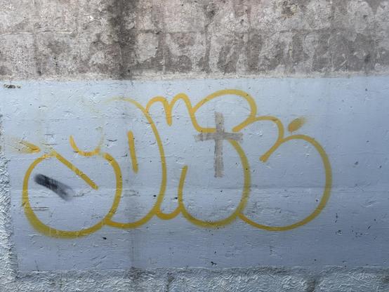 Chunky yellow graffiti with a cross slapped on a little bit of it