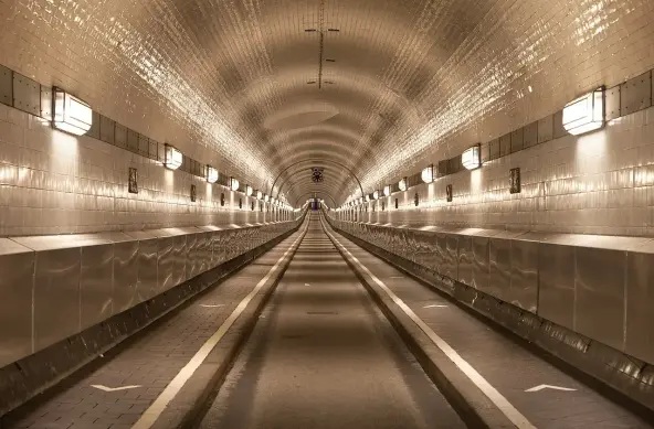 The image shows a long tunnel with a smooth, arched ceiling and tiled walls. It is well-lit, with light fixtures lining the sides. The tunnel appears to be straight and symmetrical, leading into the distance. The floor is smooth and has markings, suggesting it may be used for vehicles or pedestrians. Overall, it has a clean, modern appearance.

Image Credits: Wikimedia / Thomas Wolf, www.foto-tw.de / CC BY-SA 3.0