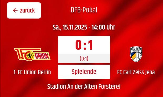 Ein rechteckiges Bild in Rot zeigt eine Sportanzeige. Oben steht in weißer Schrift "DFB-Pokal" und darunter "Sa, 15.11.2025 - 14:00 Uhr". In der Mitte steht groß "0:1" darunter in kleinerer Schrift "(0:1)". Unterhalb der Punktzahl stehen drei orangefarbene Rechtecke nebeneinander mit den Bezeichnungen "1. FC Union Berlin", "Spielende" und "FC Carl Zeiss Jena". Links befindet sich das Logo von 1. FC Union Berlin, rechts das Logo von FC Carl Zeiss Jena. Am unteren Rand steht in weißer Schrift "Stadion An der Alten Försterei". Auf der linken Seite des Bildes befindet sich ein Pfeil, der mit dem Wort "zurück" beschriftet ist.