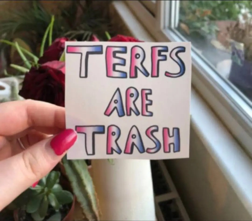 A hand holding a paper with in colourful letters "TERFs are trash" written on it