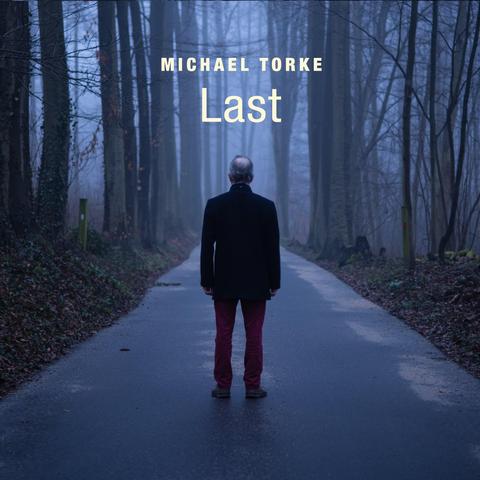 Cover of Michael Torke's Ecstatic Records album "Last", featuring an image from behind of a man standing on a country road, with trees on either side. There is fog and subdued light.