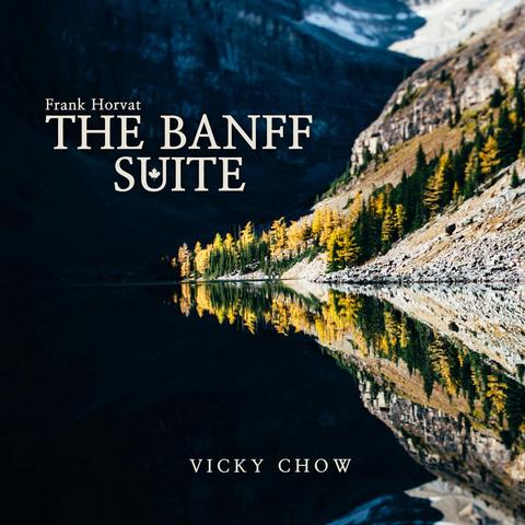 Cover of Frank Horvat and Vicky Chow's Redshift Music album "The Banff Suite", featuring a photo of a rocky mountainside with some trees, perfectly mirrored in a still lake - but where sunlight only reaches the hillside, and the entire left of the image is in total blackness.
