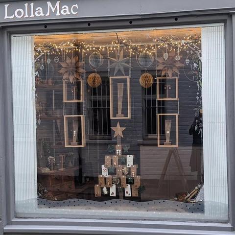 Front view of the shop window, with fairy lights at the top, paper stars and baubles, hanging wooden boxes with jewellery items on stands, and Christmas tree shaped displayed stand at the bottom