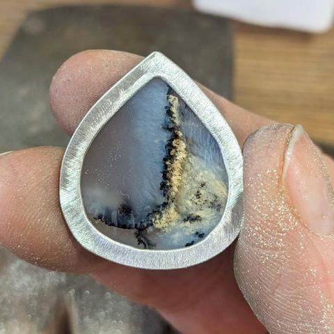 Another view of the rear of the dendritic opal in an open-backed setting, held by grubby fingers