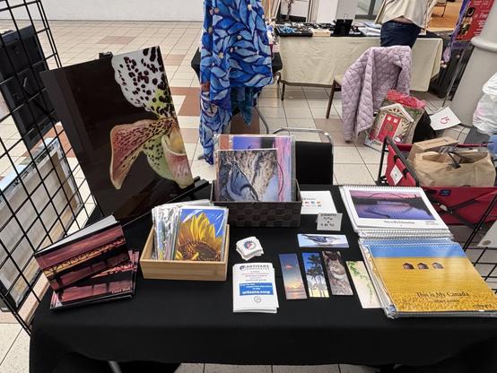 Close up of the display table for Photos By Gina, with notebooks, calendars, bookmarks, and loose prints.
