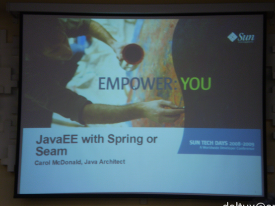 Uma tela de projeção com o início de uma apresentação com destaque de uma mistura de uma Fotografia de uma pessoa pintando uma parede com a inscrição "empower: you", o logotipo da empresa Sun no canto superior direito e, abaixo da fotografia, o título: JavaEE with Spring or Seam. Carol McDonald, Java Architect. Sun Tech Days 2008-2009. A worldwide developer conference.