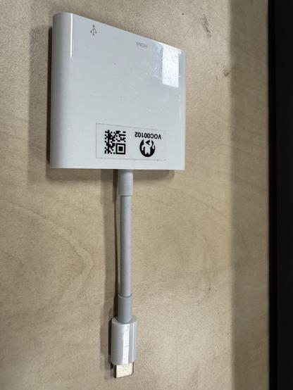 A white USB-C to HDMI/USB/USB-C converter thing marked by C3VOC is laying on a beech colored table