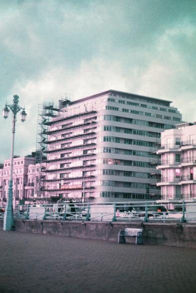 The front of embassy court lit up with the setting sun, which is shifted to purple, thanks to the film stock, there is one of the streetlights and the blue metal railing in the foreground