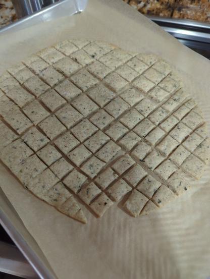 A tray of sourdough crackers. It looks like a flat round of dough was cut into bite-size squares, on a sheet of parchment paper.