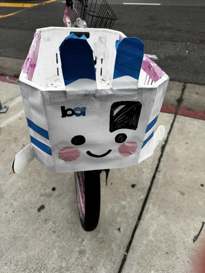 A rear basket on a bicycle decorated like an anthropomorphic BART train car with rabbit ears.