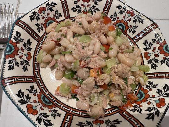 Salad on a plate with stylized design of black leaves and red and green flowers.
