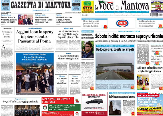 Prima pagina di giornale proiettata su uno schermo in una stanza buia. Si vedono due testate: "Gazzetta di Mantova" e "La Voce di Mantova". I titoli principali menzionano temi di attualità locale, come attacchi con spray urticante in centro città, mercatini di Natale e cronaca. Tra i titoli leggibili: "Agguati con lo spray in pieno centro Passante al Poma", "Sabato in città: maranza e spray urticante". Sono presenti anche alcune foto di persone ed eventi locali, annunci pubblicitari e rubriche istituzionali.