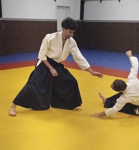 Me wearing white keikogi and blue hakama, on a yellow tatami. Dynamic pose after throwing an aïkido partner to the ground.