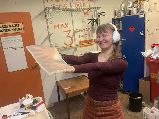 Kaisla pitelee ylpeästi, kuin Simbaa Jylhäkalliolla, käsissään paksua läpinäkyvää muovilevyä. Taustalla näkyy värikäs yhteinen Hacklabin maalaamo. Kaislalla on riemukas virne kasvoillaan, ja vastamelukuulokkeet päässään.