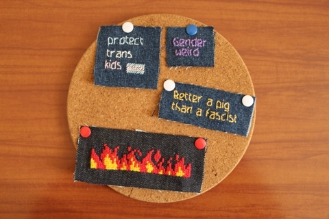 Photo de 4 patchs en jean brodé : trois avec des textes
- "protect trans kids "
- "gender weird "
- "better a pig than a fascist"
et un avec des flammes en point de croix