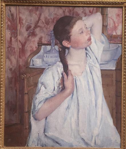 From the museum plaque: This young woman sits at her dressing table arranging her hair. She is looking at herself in a mirror just outside the frame. Cassatt is referencing a popular tradition in European painting: male artists depicting women dressing or undressing.
These works show erotic fantasies of women in private spaces. By contrast, Cassatt's sitter is enjoying a peaceful moment of self-regard. Her ruddy complexion, large teeth, and recessed chin do not match beauty ideals of the time.
The carefully drawn pose and richly painted white shirt are set against fantastic pink, red, and mauve wallpaper. They signal the care Cassatt took with this portrait, among the most accomplished in her career.