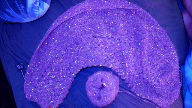 half round shawl and winded yarn, the yarn is purple and has neon bits that shine under uv light. all is somewhat blueish from the uv light