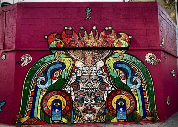 Urban mural in Mexico City, depicting pre-Hispanic motives made with reclaimed ceramic tiles on a magenta wall.