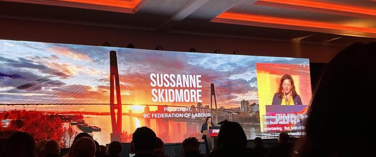 A large wide screen shows a sunrise over the Port Mann Bridge and Fraser River
