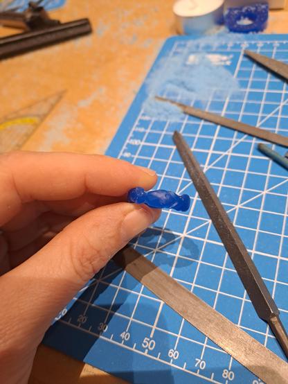 A close up,  fingers holding the carved wax blank. Theres not enough detail to tell what it is, but its a series of misshapen fish following one another around the band