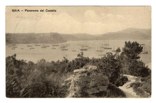 The image depicts an old black and white photograph of a harbor scene with numerous sailboats anchored in calm waters. In the foreground, there is a natural landscape featuring dense vegetation, including shrubs and trees, which suggests that this viewpoint might be from atop or beside a hillside covered in foliage. A prominent stone structure resembling part of a wall or fortification can also be seen near the bottom right corner.

The middle ground shows a serene harbor with several sailboats moored at various distances, creating an expansive maritime panorama. The background features gentle hills or mountains faintly outlined against a soft horizon line under a sky that appears overcast but not heavy with clouds.

At the top of the image, there is text in Italian: "BAIA - Panorama dal Castello," which translates to "Bay – Panoramic View from Castle." This suggests that the vantage point for capturing this photograph was possibly on or near an elevated structure like a castle. The overall scene conveys a sense of historical context and picturesque seaside charm, indicative of Bacoli Bay's scenic appeal as captured in past photographic documentation.

Additional information about this image can be found at: https://images.loener.nl/FerroCandilera/full/6730/6730981a89b10e7a26b638ff.jpg, which may provide further details on the photographer or context of the photograph.