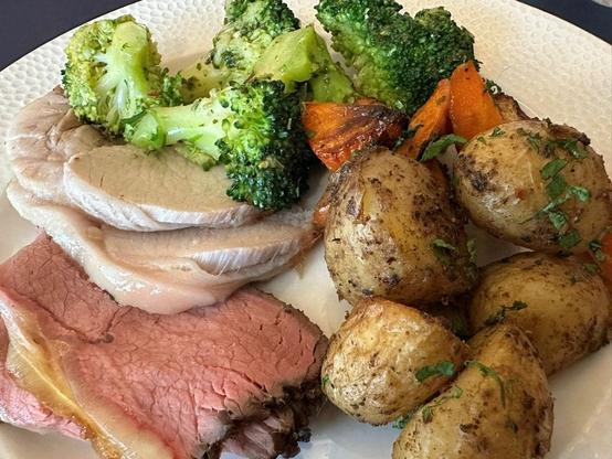 Plato con lonchas de cerdo asadoy de ternera, brócoli, zanahorias y patatas asadas con piel, decoradas con perejil.