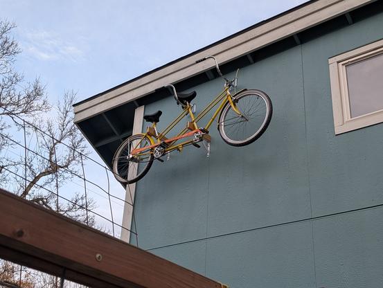 A blue garage with a yellow tandem bicycle hung up as a sculpture.
