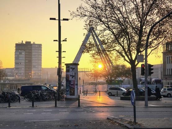 Ein noch im Aufbau befindliches Riesenrad vor dem Kieler Hauptbahnhof. Zwischen den Stützen geht die Sonne auf.