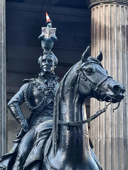 A statue of the Duke of Wellington in Glasgow, with a pigeon wearing a road cone attached to its head.