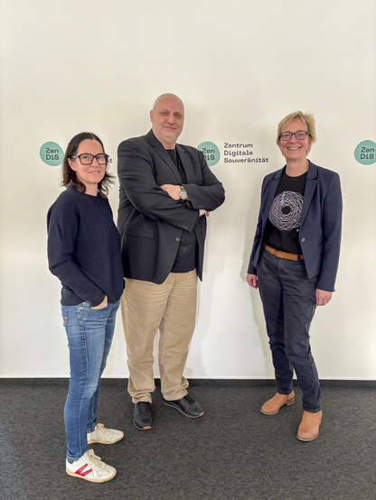 Pamela Krosta-Hartl, Alexander Pockrandt und Christine Regitz stehen vor einer Wand mit ZenDiS-Logos.