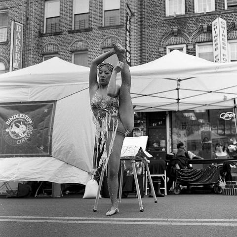 black and white image of a contortionist woman performer, standing on one leg with one leg up in the air