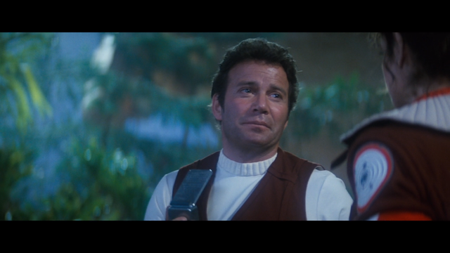A shot from Star Trek II: The Wrath of Khan showing Kirk with a confident look on his face holding his communicator and talking to Saavik.  They are in the Regula I Genesis cave.