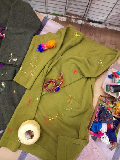 Sweater with colourful wild embroidery. The holes are repaired in yellow and orange but intuitive stitching in these colours connects them, "painting" stars, butterflies (moths?), lines.