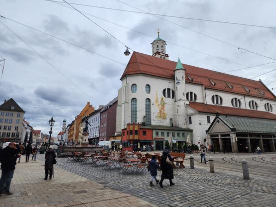 Cobblestone street in a German city center. At center in the distance is the white and minimalist exterior of the church, sporting a red roof and the same circular designs in the windows described in the posts above.