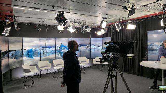 Kamalan paljon valoja ja taustapanelissa jäätiköt ovat sulamassa, edessä prompterikamera.