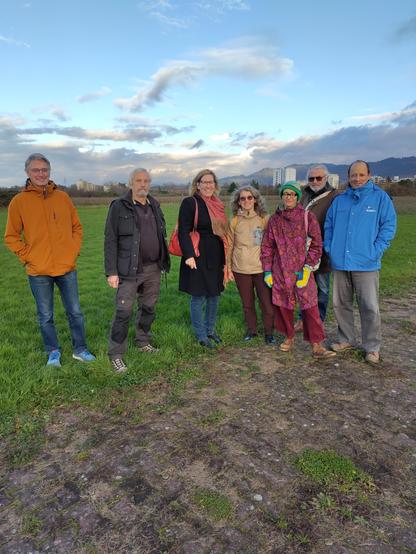 Ein Gruppenbild vom Flughafen, links zwei Menschen aus der Fliegergruppe, dann Maren Seifert, rechts vier Menschen von BUND und NABU. Wir stehen auf der Wiese, im Hintegrund erkennt man Hochhäuser der Stadt Offenburg, der Himmel ist wolkenverhangen. Trotz ernster Themen wird gelächelt, dass Wetter wirkt freundlich und frostig zugleich. Alle sind farbenfroh gekleidet.